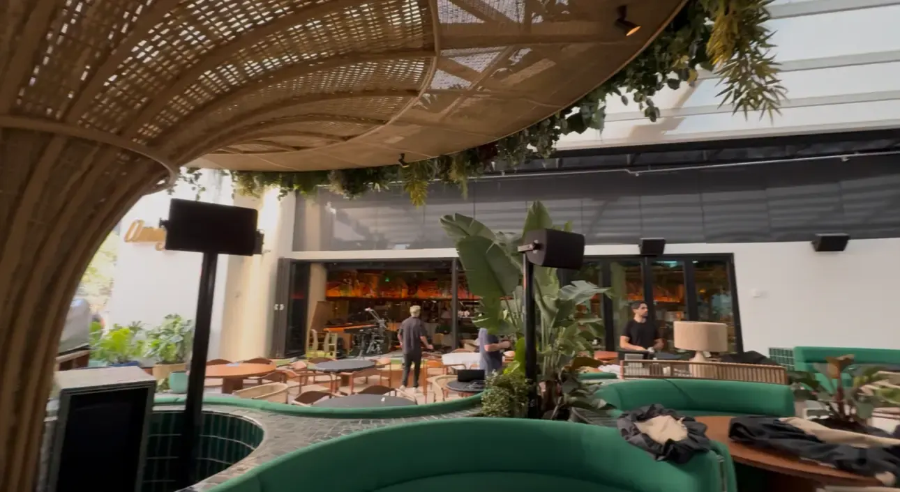 Amazonico restaurant terrace in Miami with pole-mounted loudspeakers above curved green banquettes under a woven canopy