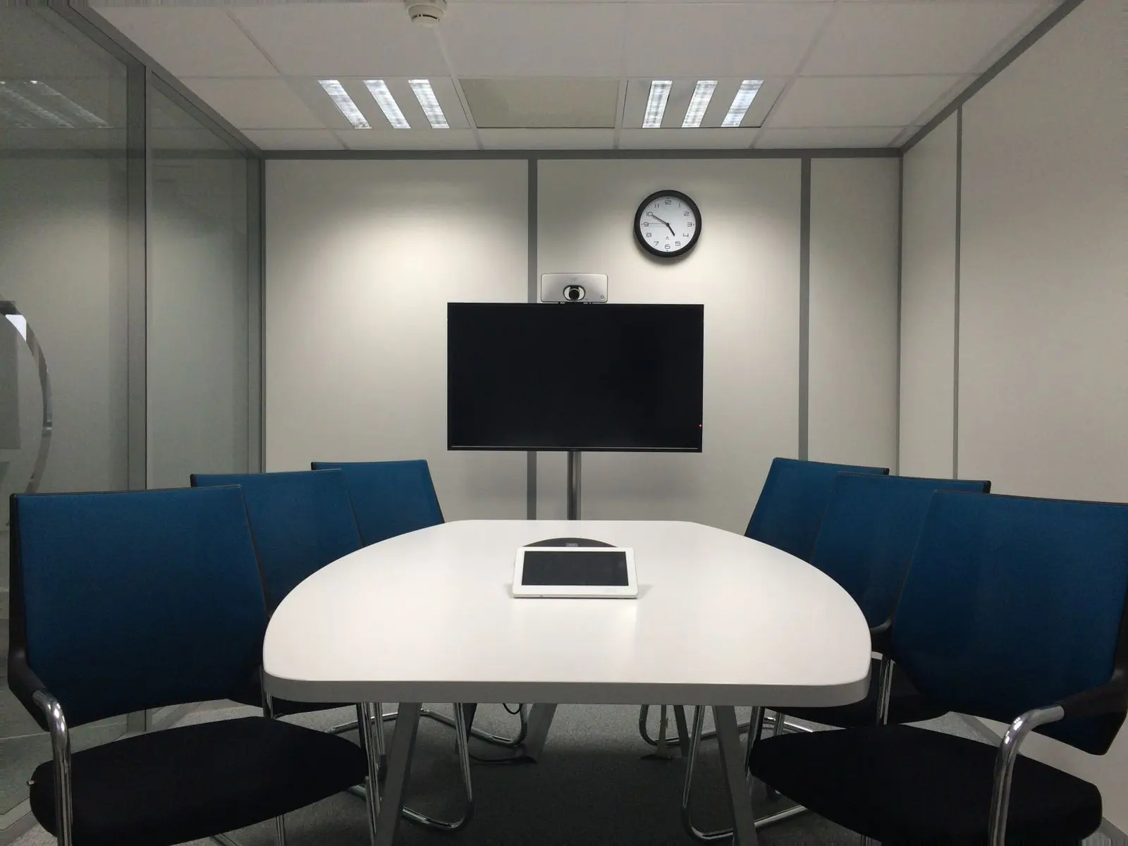 Conference room with a wall-mounted display, camera above it and a tabletop touch console