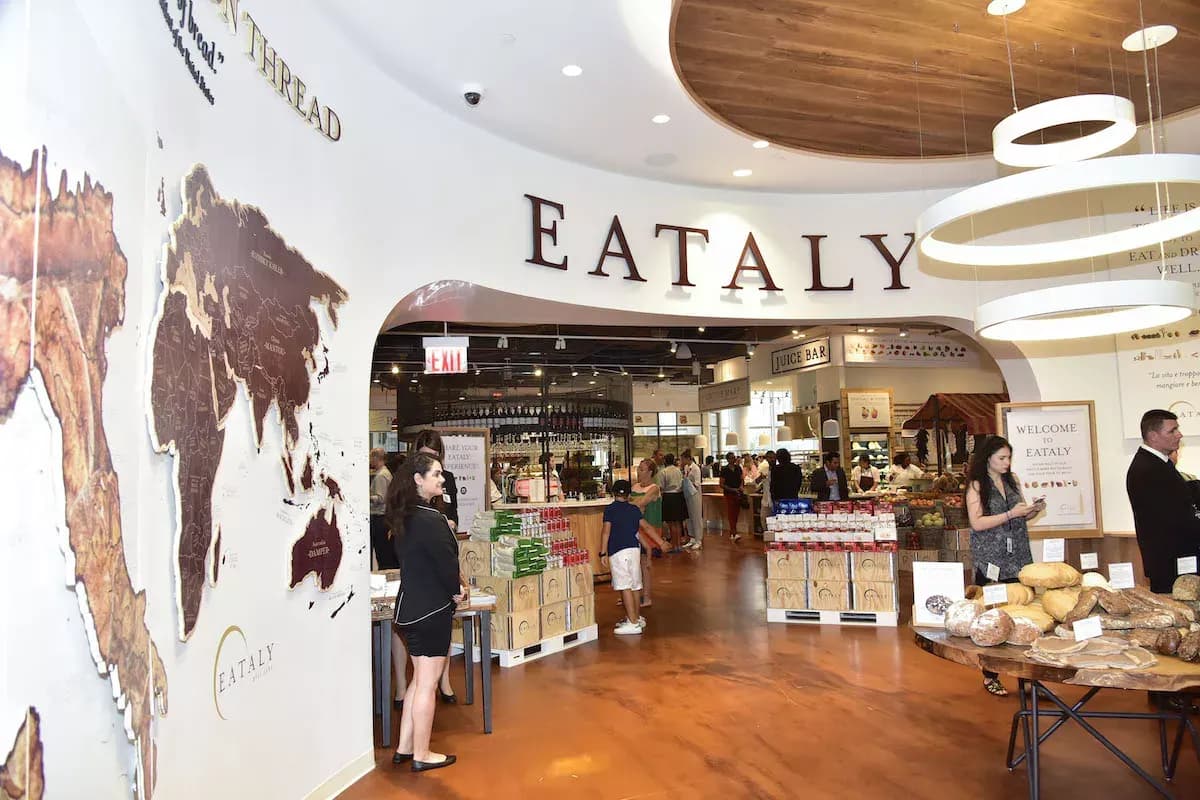 Entrance area of the Eataly Aventura marketplace with the Eataly sign, world-map wall mural and shoppers