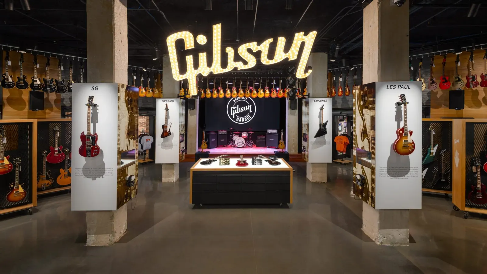 Interior of Gibson Garage with the illuminated Gibson sign, guitar displays and a stage with drum kit at the far end