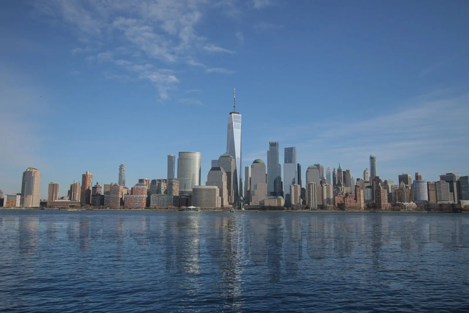 Lower Manhattan skyline seen from the harbor under a blue sky
